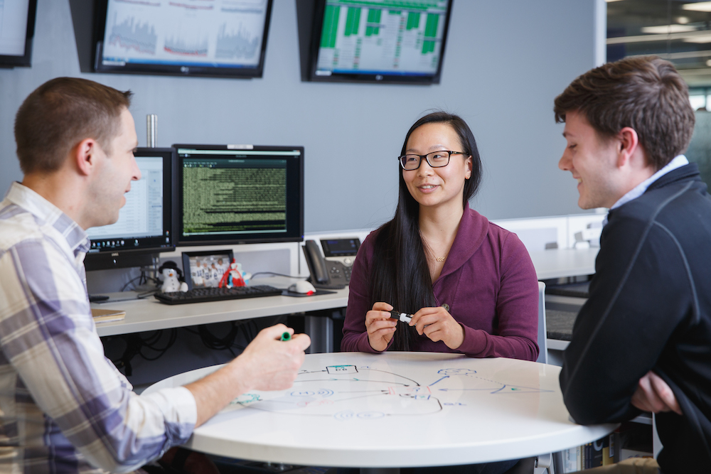 A woman and two men sitting around a table talking in an office.