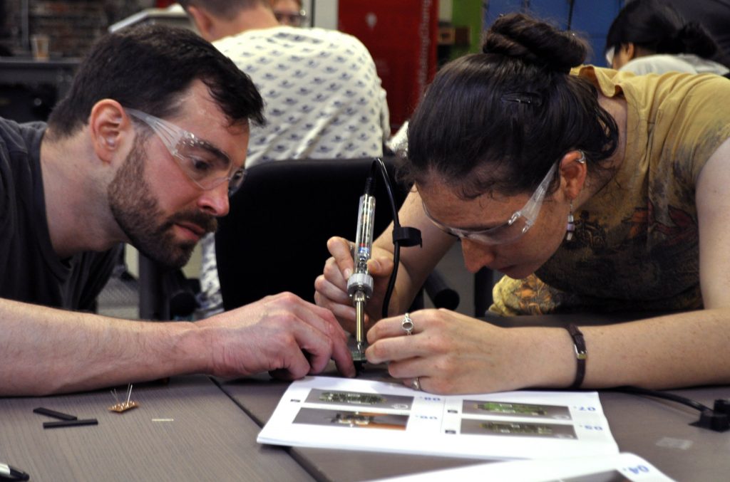Two people using a soldering iron