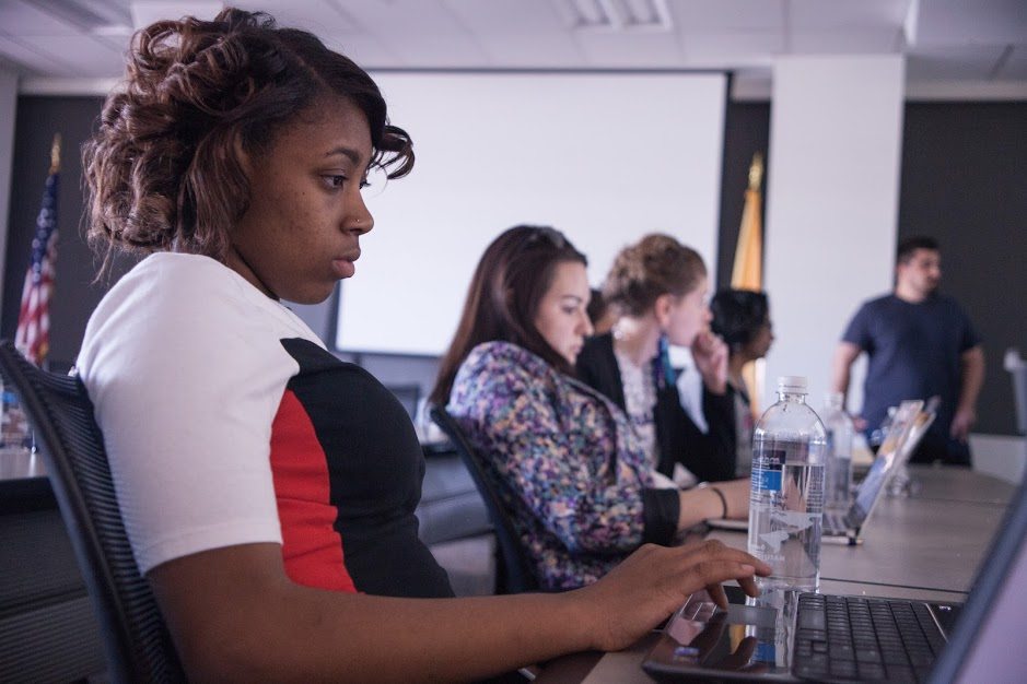 Three girls sitting and typing in a classroom setting.