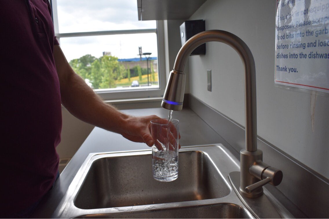 A person pouring a glass of water using a silver faucet.