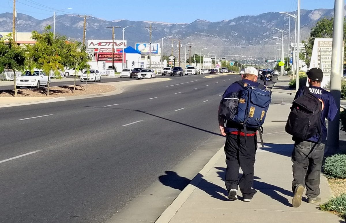 Two men walking by the side of the road.