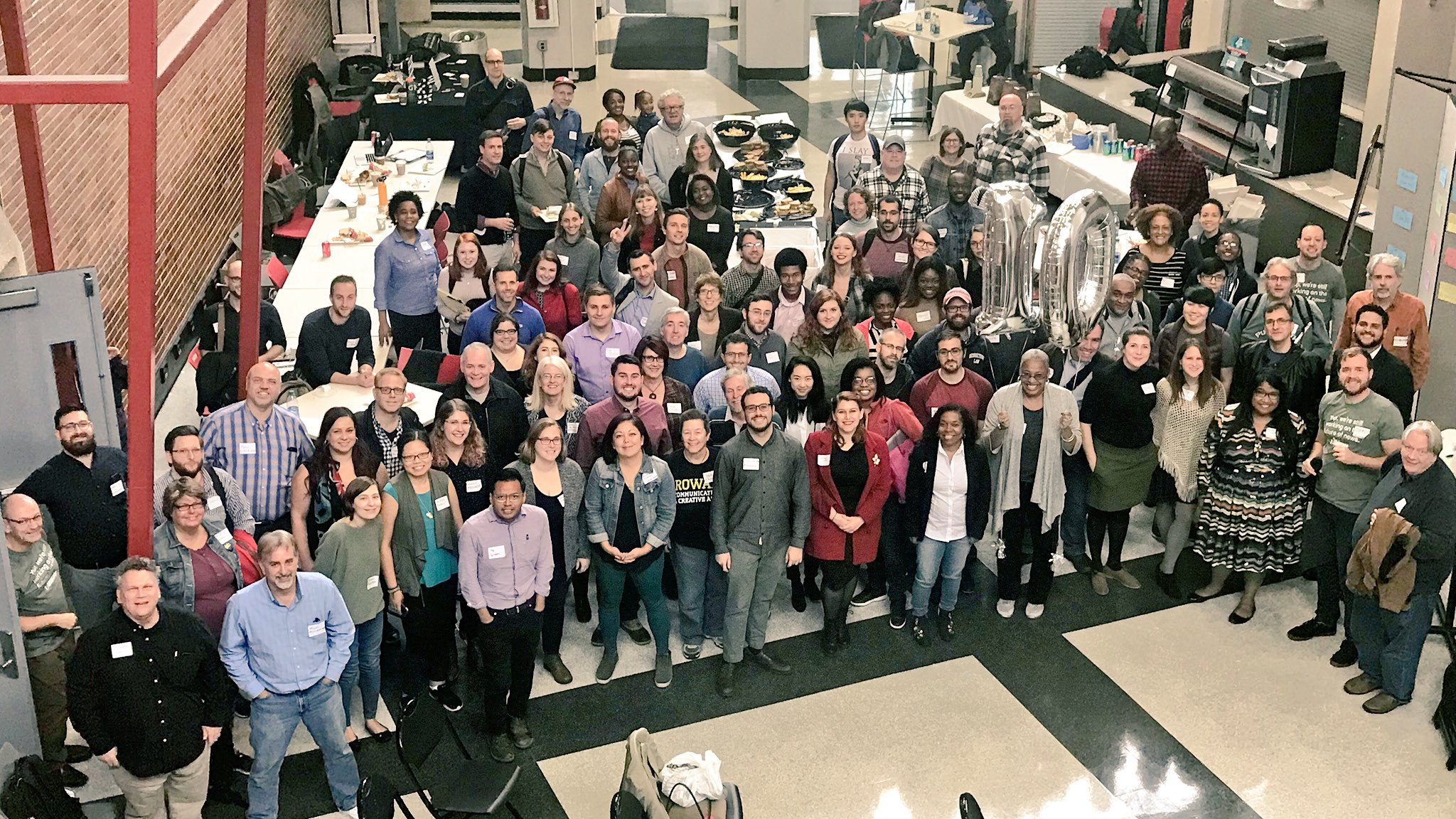 A large, diverse group of people posing for a group photo in a brightly lit indoor lobby or event space.