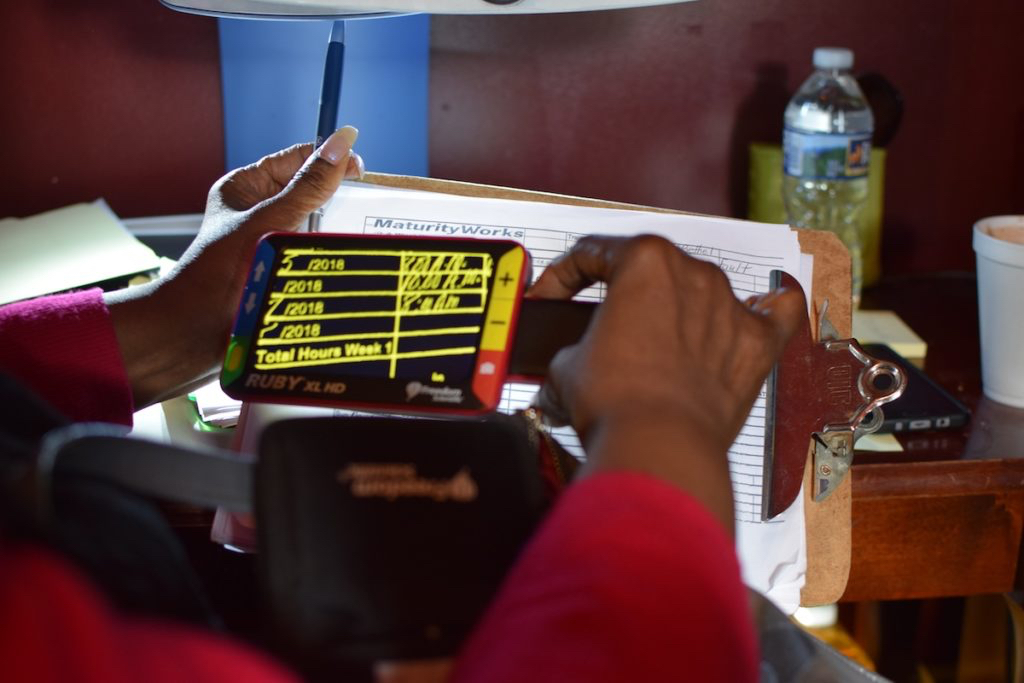 A woman holding a screen reader over a piece of paper to better read it