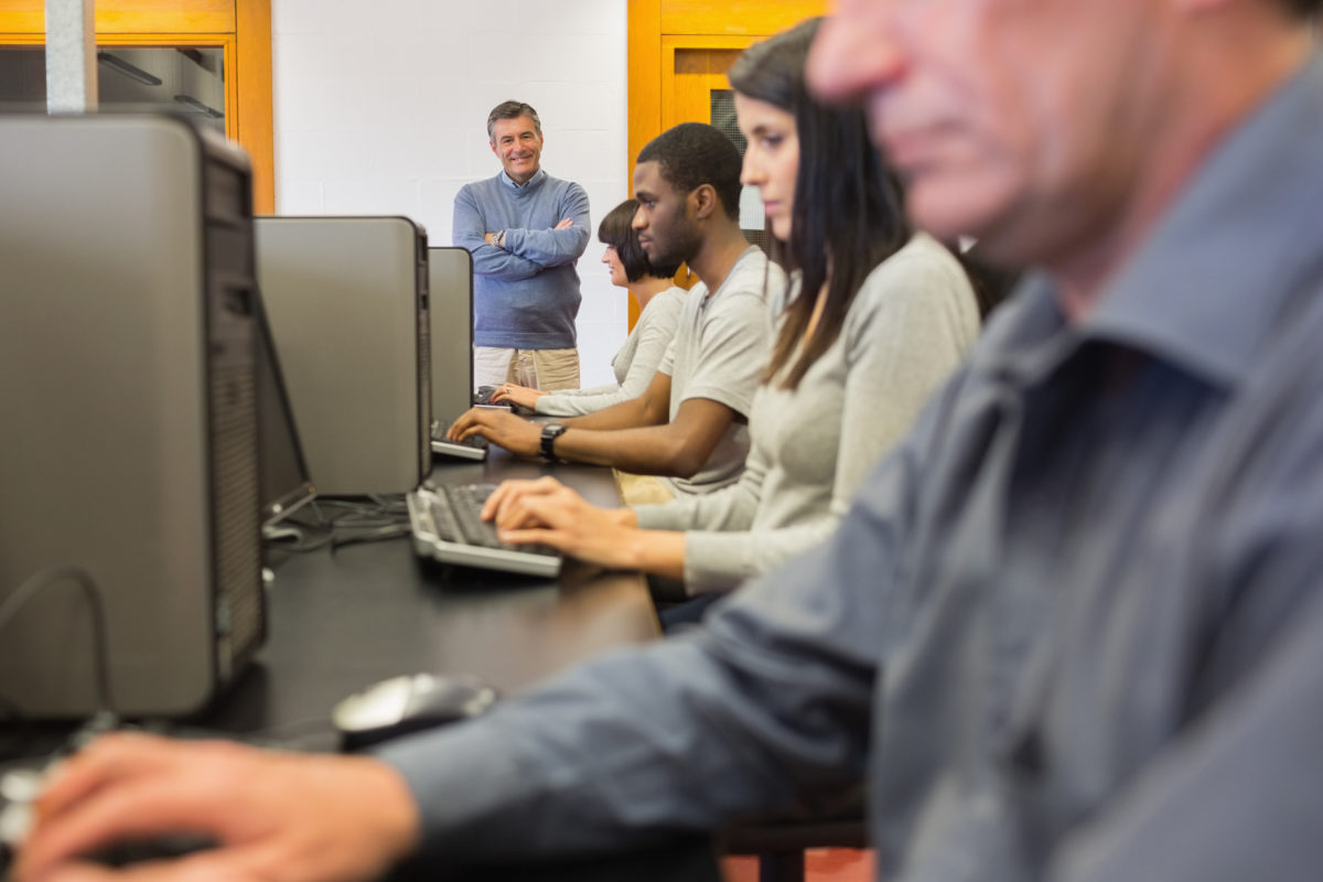 Teacher standing at front of computer class with arms crossed