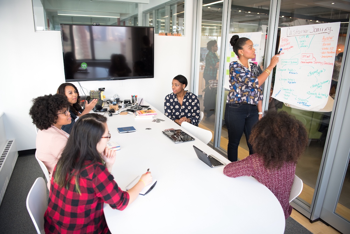 Five women sitting around a conference table while one woman presents