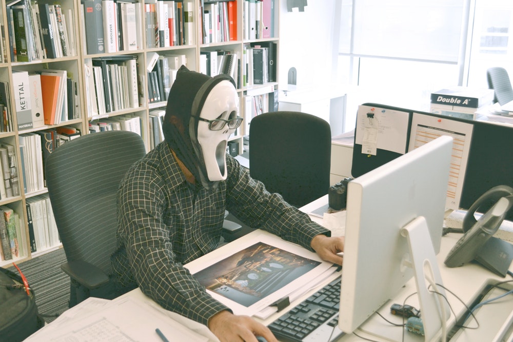 Person in Scream mask using a computer.