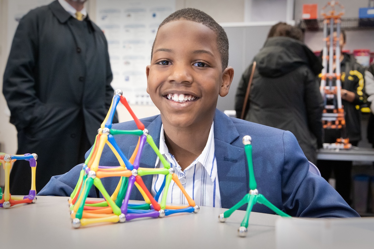 A boy smiles in front of a STEM puzzle