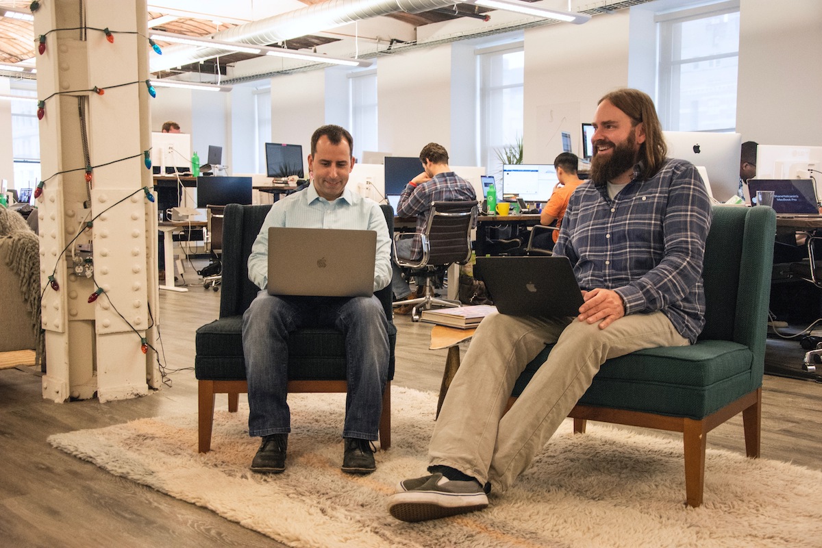 Two men sitting in chairs with laptops on their laps.