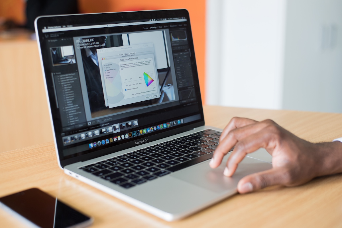 A person touches a laptop displaying graphic design images