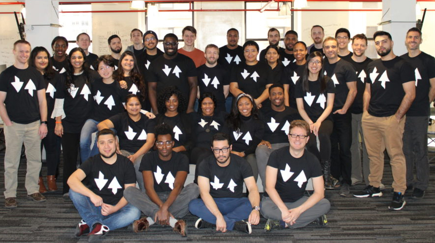 A group of coding students in black shirts with white logos
