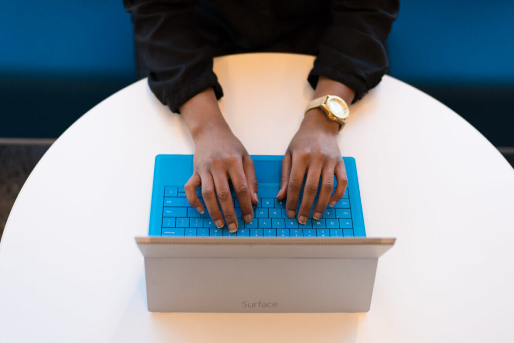 A woman's hands type on a blue keyboard. Her face is not visible.