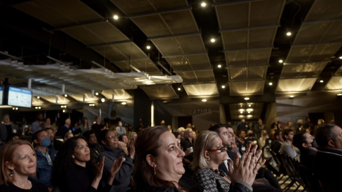 Crowd of people clapping in dark-lit room.