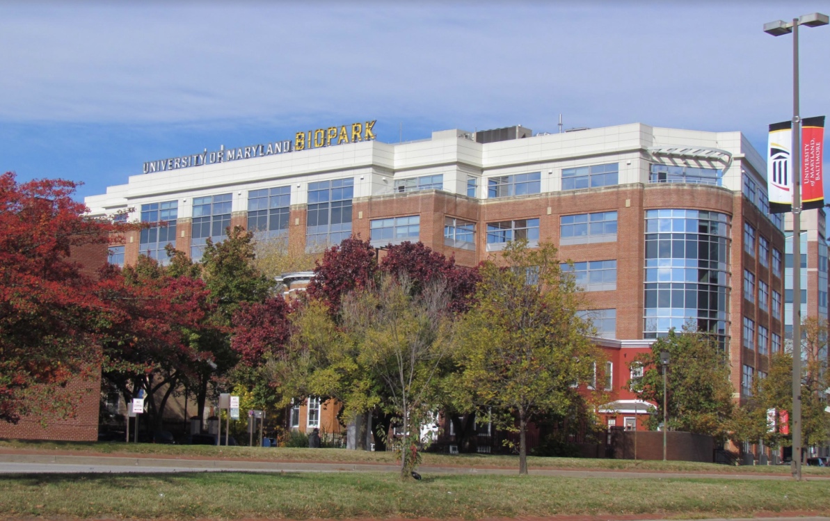 A multi-story brick and glass building labeled “University of Maryland BioPark” stands behind trees with autumn foliage.