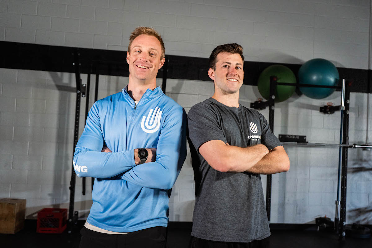 Two men stand and smile with their arms folded