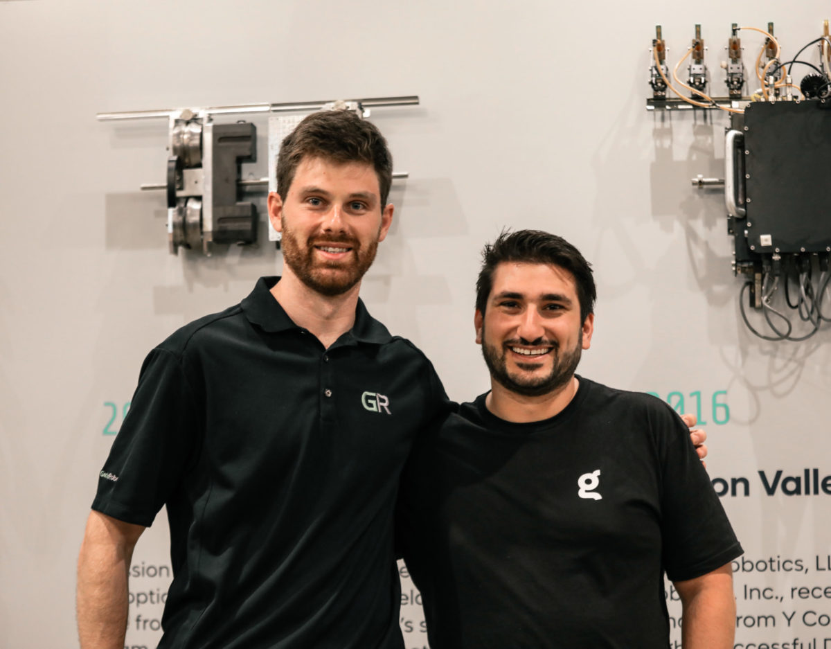 Two men standing next to each other in front of a wall.