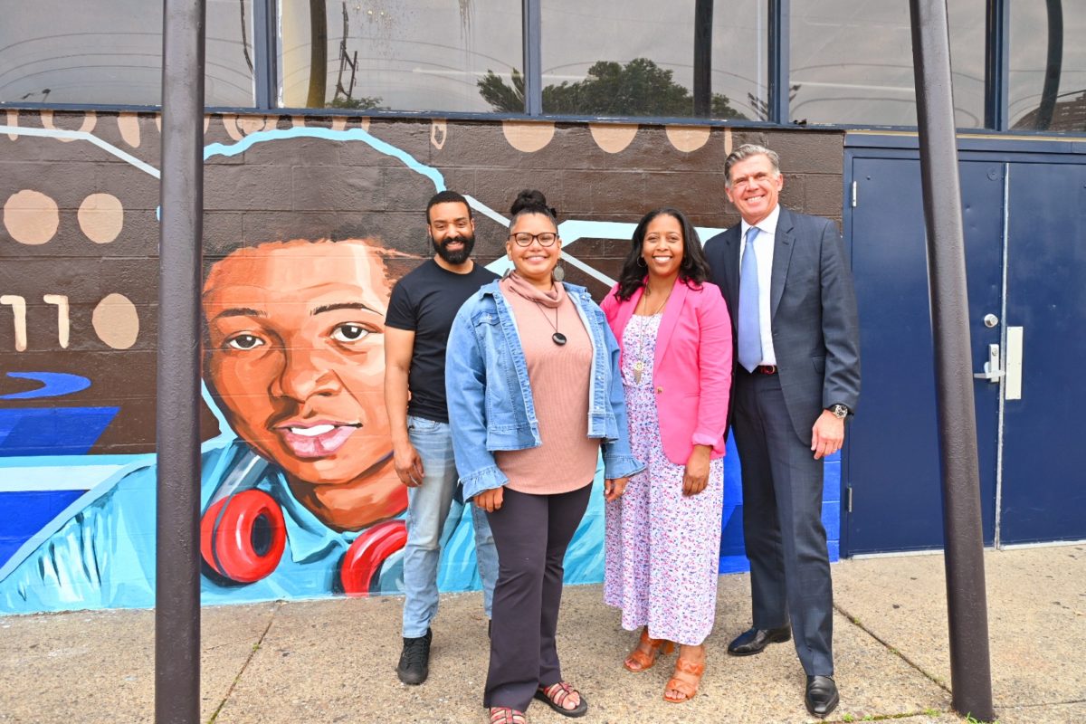 Four people pose in front of a mural at Smith playground.
