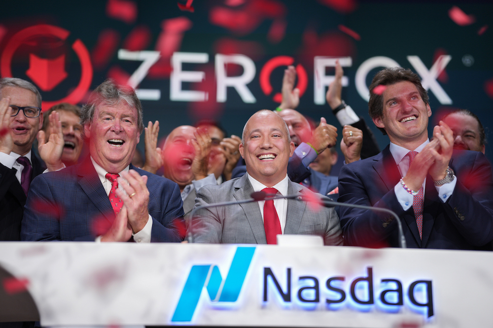 ZeroFox staff in front of logo behind Nasdaq desk as red ticker tape falls.