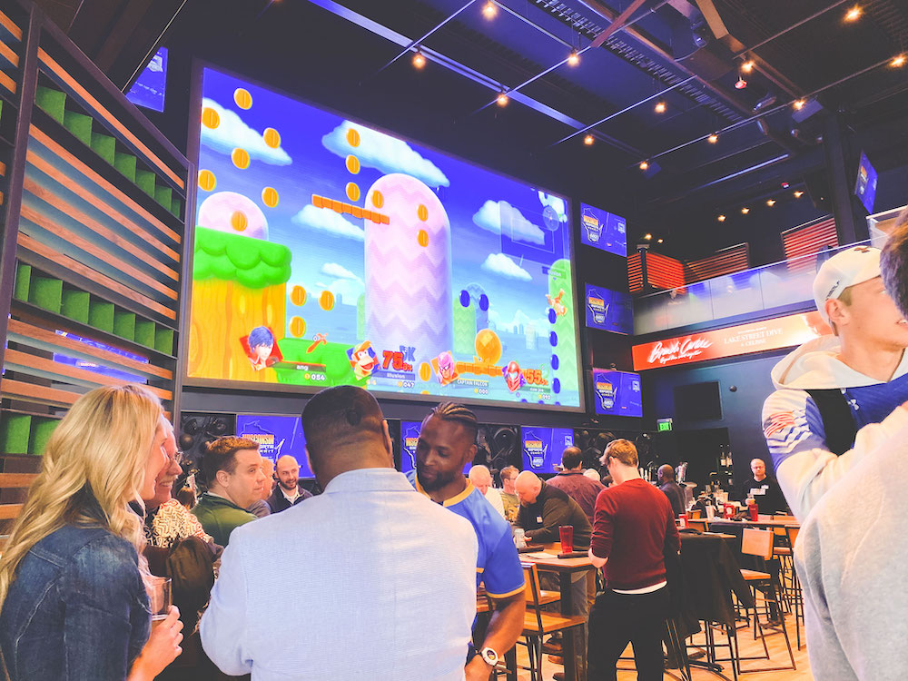 People watch a Nintendo eSports game on black projector against blue and orange striped wall