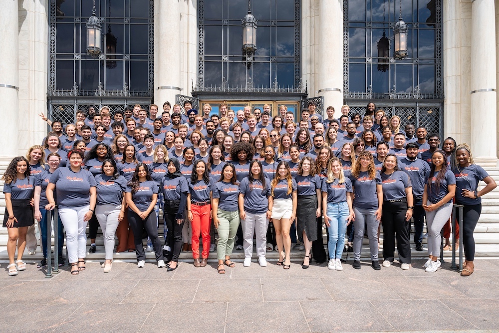 group poses in navy shirts in front of cream building on brown concrete