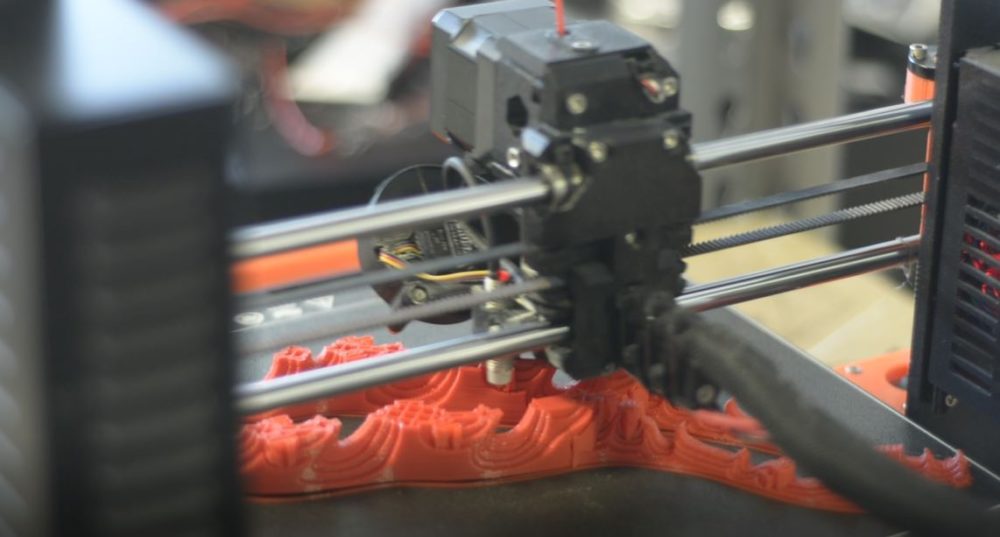 Black 3D printer with grey components makes orange