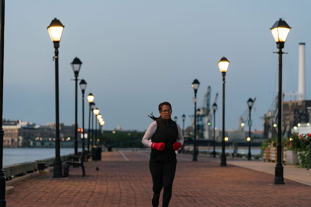 Woman in red gloves and black and grey workout clothes on red brick pier in front of grey sky