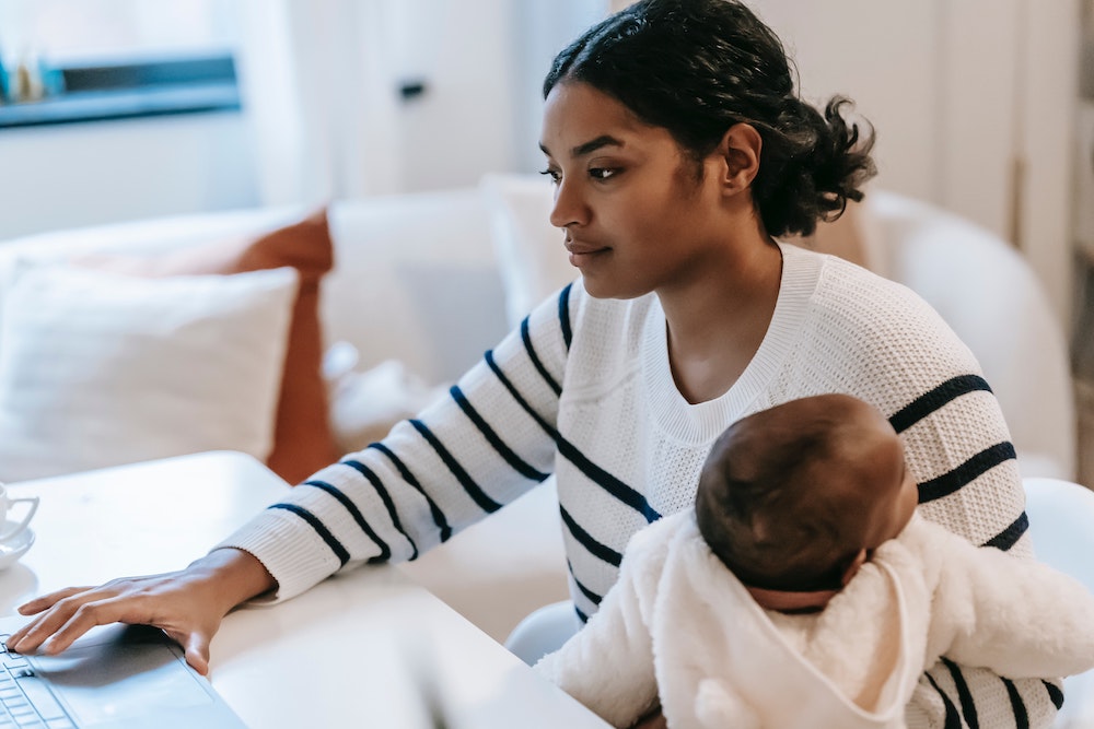 Woman holds baby while working at white desk in front of white furniture