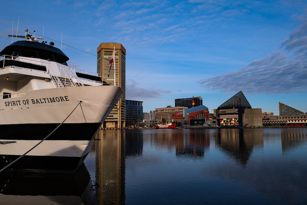 Baltimore skyline against blue sky and water with Spirit of Baltimore ship.