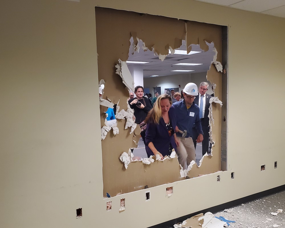 People barge through hole in brown wall