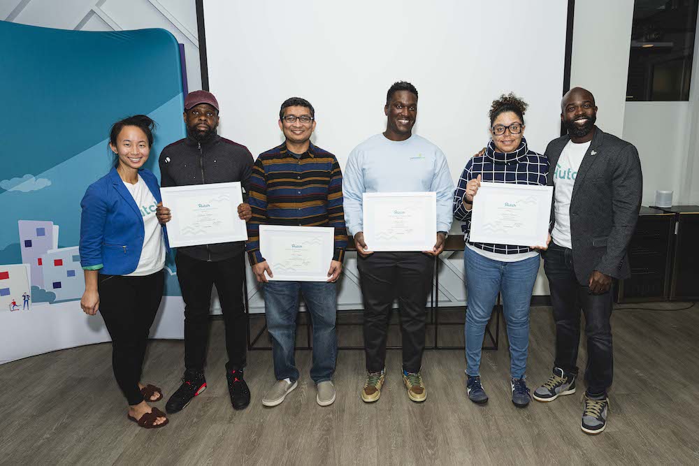 Women and men pose while holding white placards with light blue text in front of white wall with blue paint