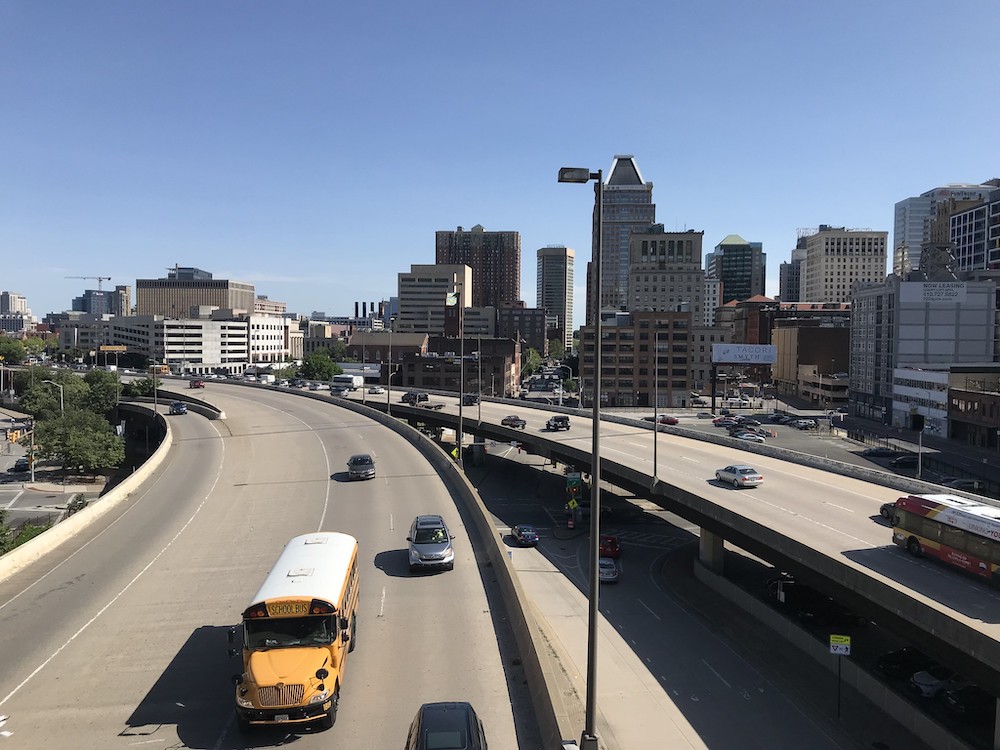 Baltimore before blue sky and behind brown highway with yellow bus.