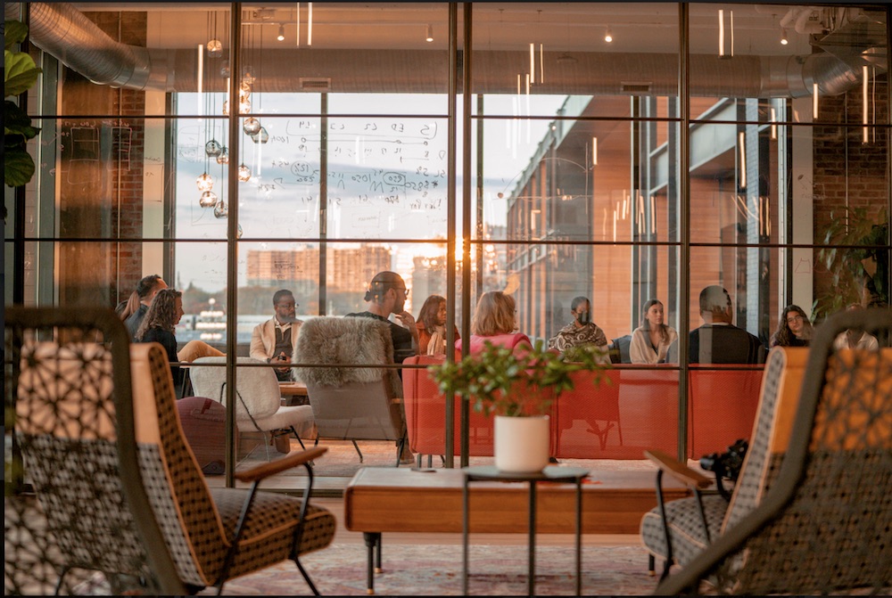 People in glass wall room on red furniture bathed in pink light