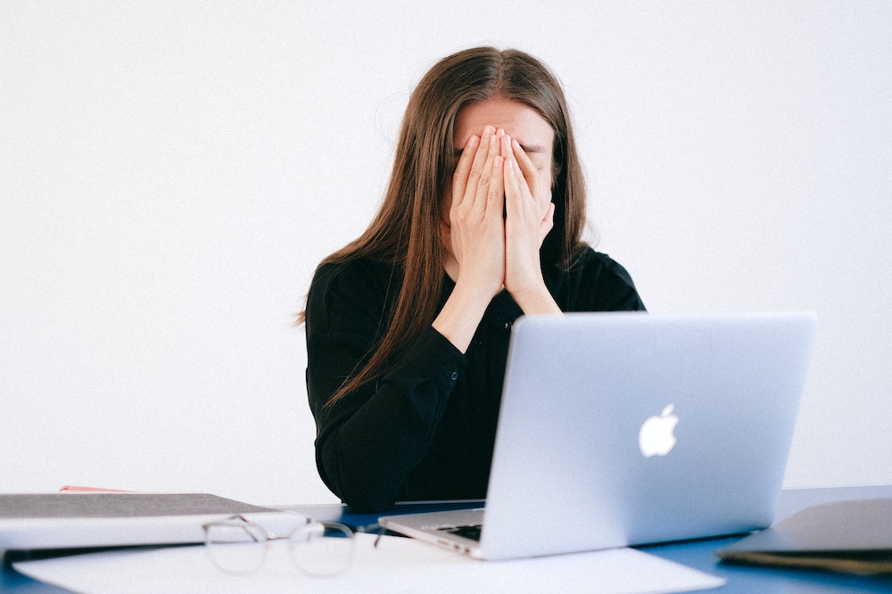 A woman sitting at a laptop covering her face.