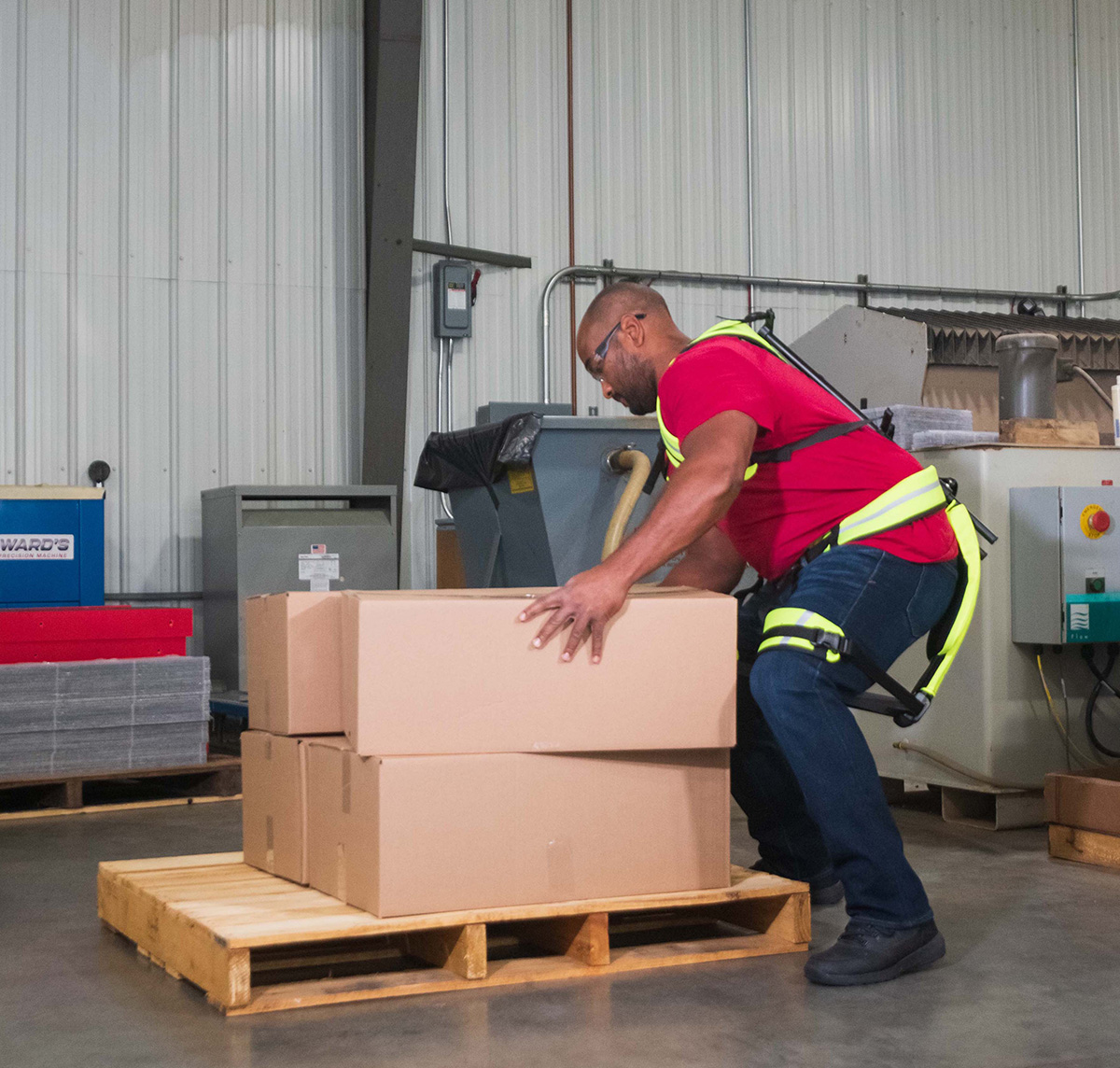 A man bending down in order to lift a box and wearing the exoskeleton.