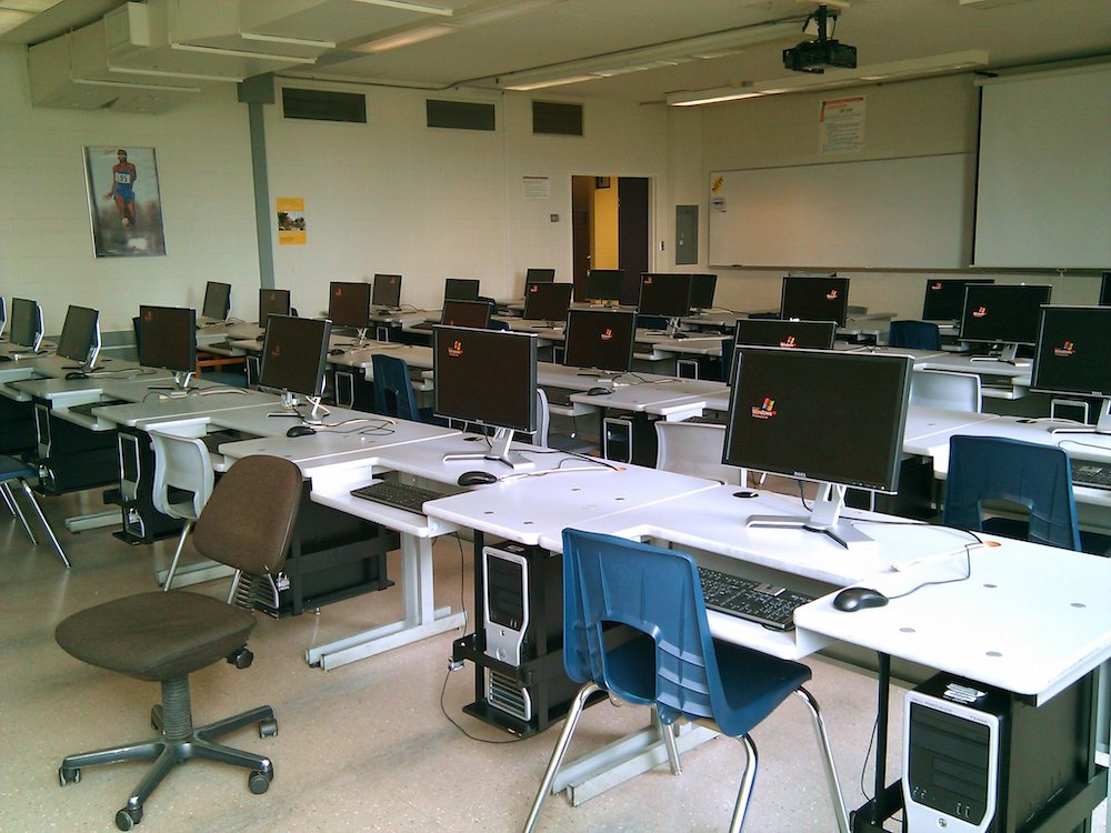 White coworking desks with black computers near blue and brown chairs.