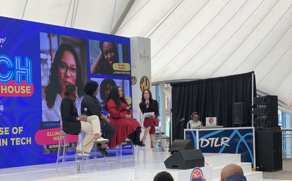 Women in red, black and white outfits speaking at panel in front of blue images