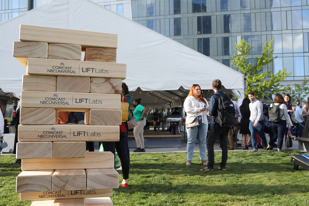Individuals in the background talking and a stack of large Jenga blocks in the foreground with Comcast logo.
