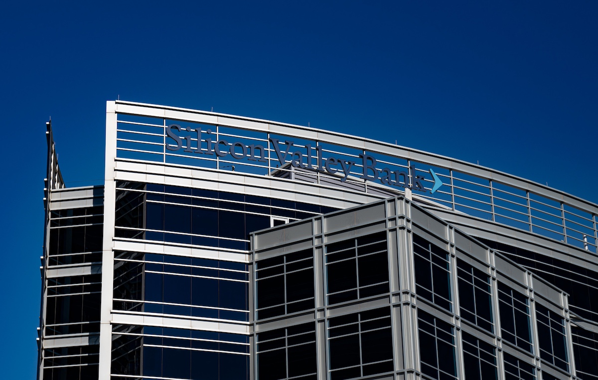 The image shows the exterior of a modern building with large glass windows, featuring the name "Silicon Valley Bank" prominently displayed at the top. The sky is clear and blue.