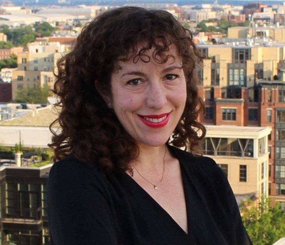 Julie Saltman smiles in brown hair and black blouse before cityscape