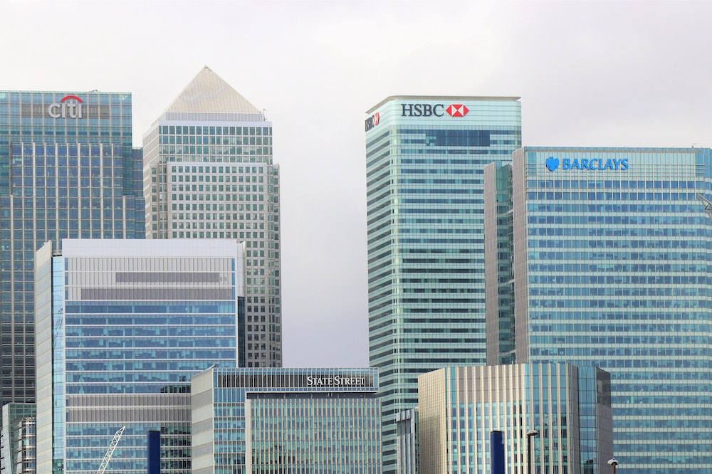 Several high-rise buildings of major financial institutions, including Citi, HSBC, Barclays, and State Street, against a cloudy sky.