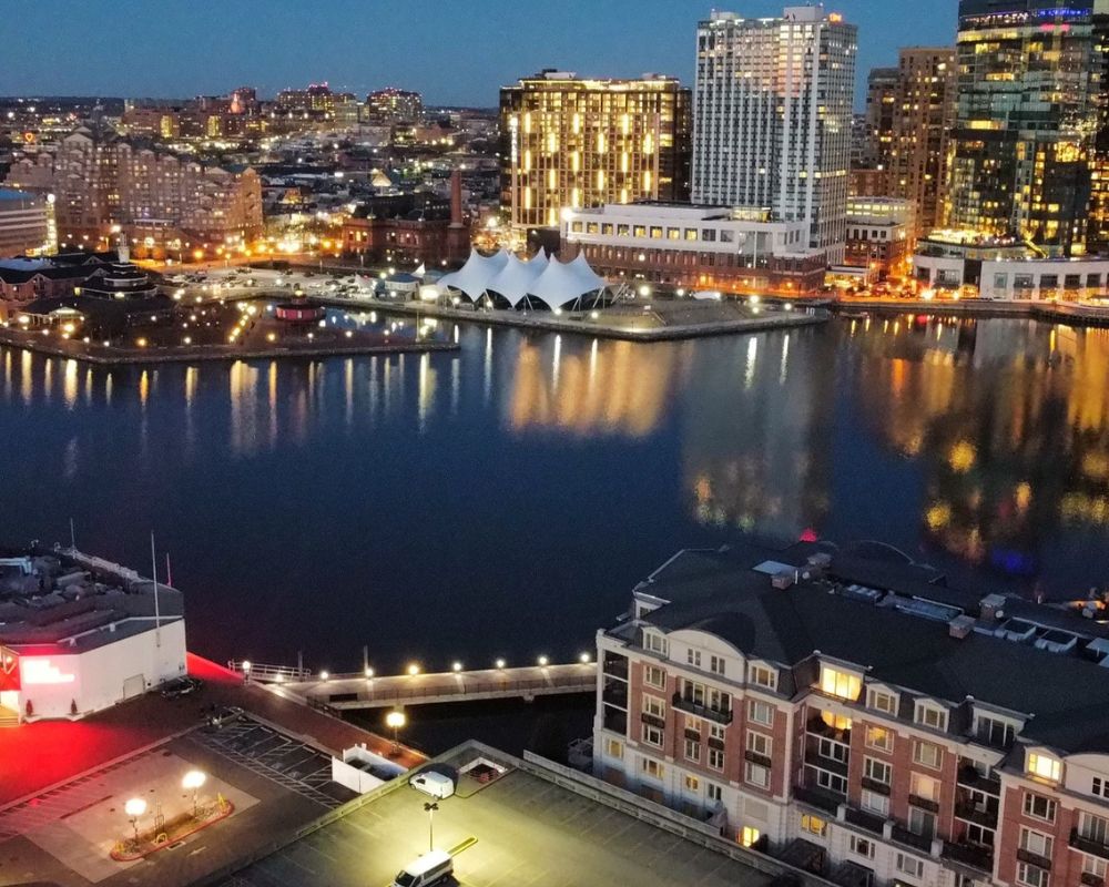 Evening view of an urban waterfront with illuminated buildings and calm water reflections.