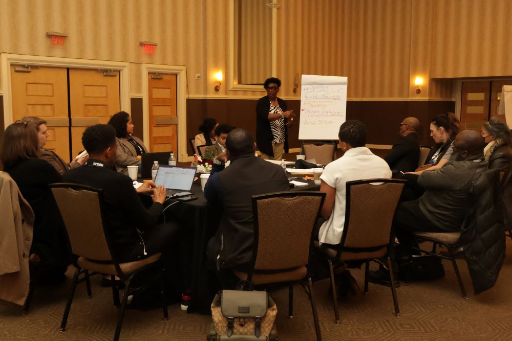 Folks sit around a table while a speaker presents with a large note sheet.