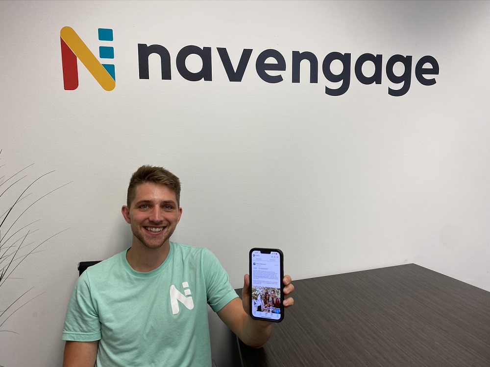 Andrew Strause holding a phone under a sign that sys Navengage.
