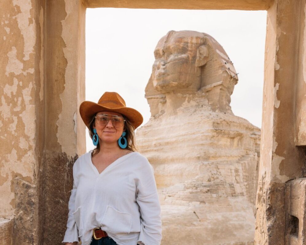 Katalina Mayorga stands in jeans and a white shirt in a doorway in Cairo. The Sphynx is in the background
