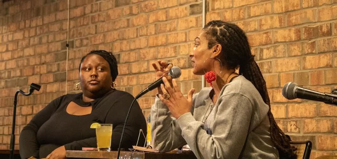 Two women participating in a panel discussion with microphones in front of a brick wall.