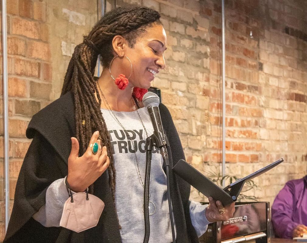 Woman speaking into a microphone while holding a tablet.
