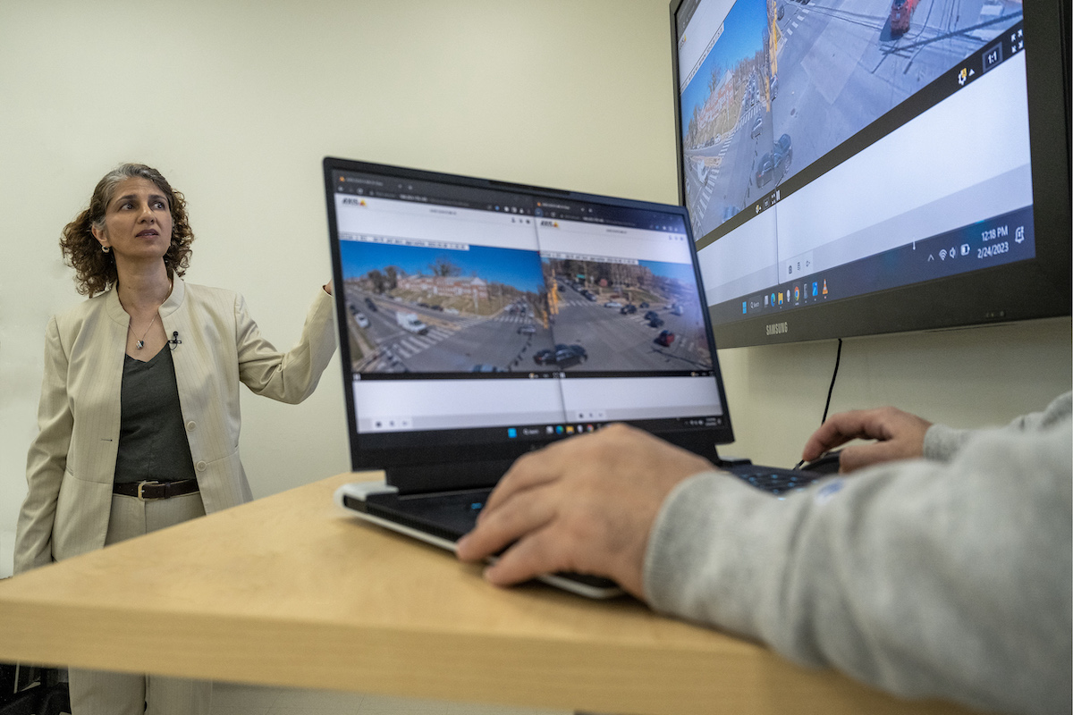 A person gesturing towards a monitor showing surveillance camera footage during a presentation or demonstration.