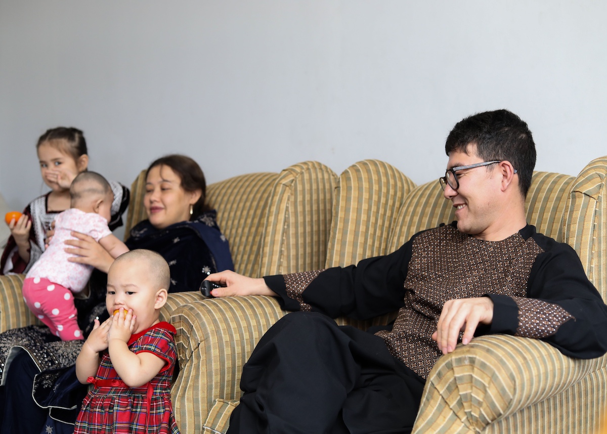 Family relaxing on a couch with young children eating fruit.