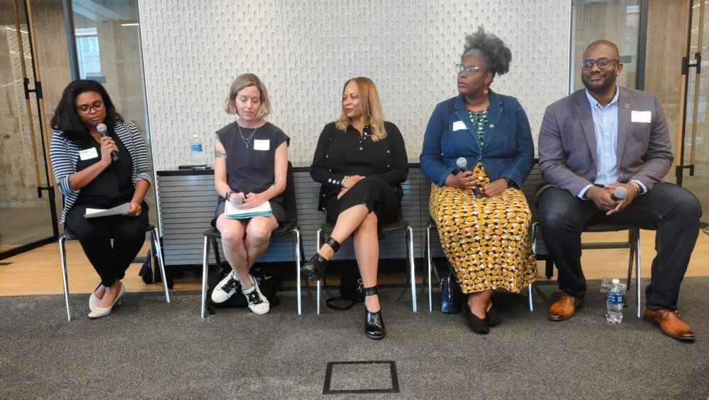 Five individuals seated on a bench during a panel discussion, with one person speaking into a microphone.