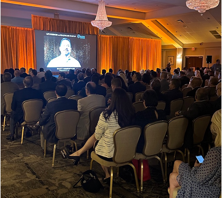 Audience attending a presentation in a conference hall with a speaker being projected on a large screen.