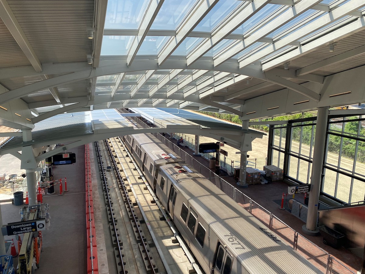 Elevated train station with a train at the platform and sunlight filtering through the roof structure.